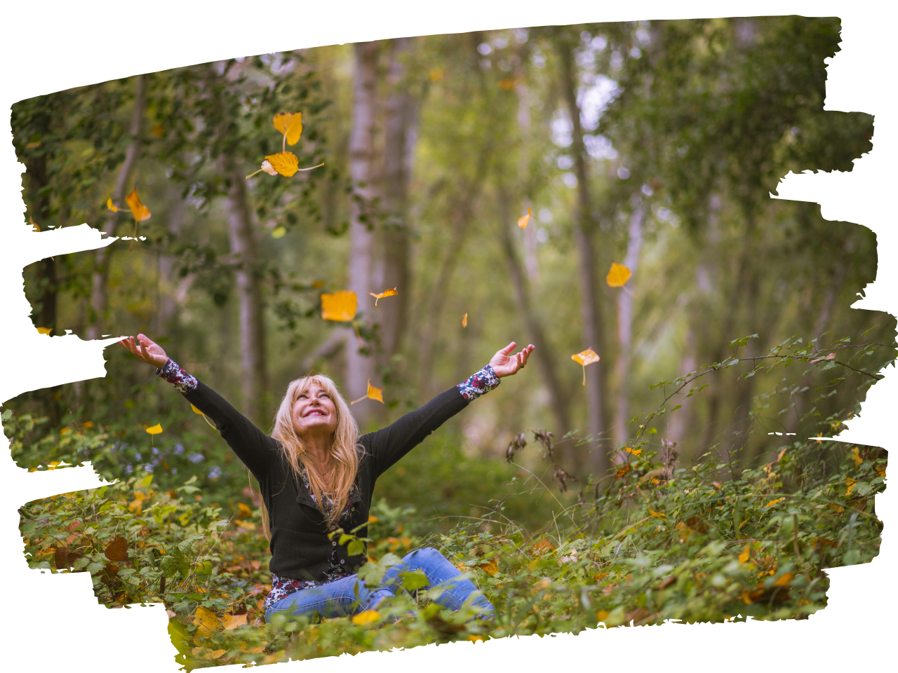 Woman sitting on ground in the woods tossing leaves into the air joyfully