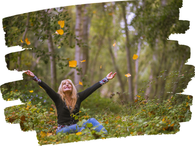 Woman sitting on ground in the woods tossing leaves into the air joyfully