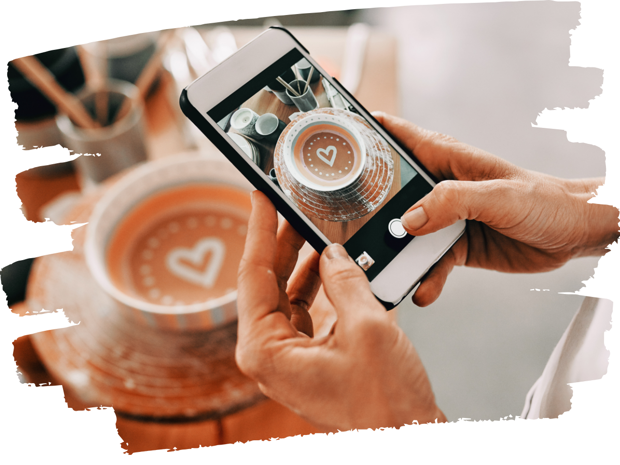 Person taking a phone photo of a ceramic pot with a heart in the bottom