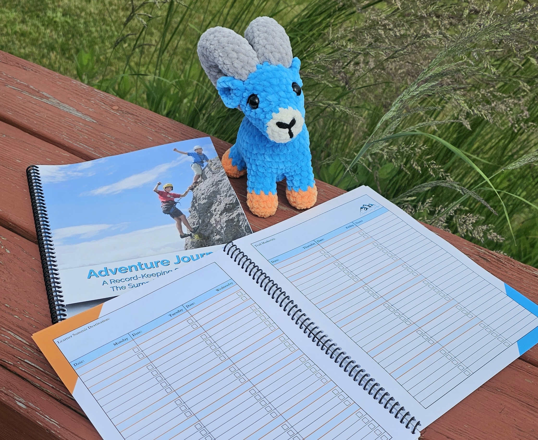 Plush bighorn sheep sitting next to Adventure Journals - one closed and one open to record-keeping pages